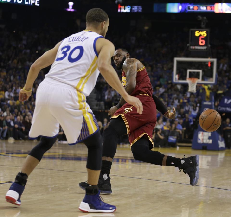 Cleveland Cavaliers' LeBron James passes behind his back away from Golden State Warriors' Stephen Curry (30) during the first half of an NBA basketball game Monday, Jan. 16, 2017, in Oakland, Calif. (AP Photo/Ben Margot)