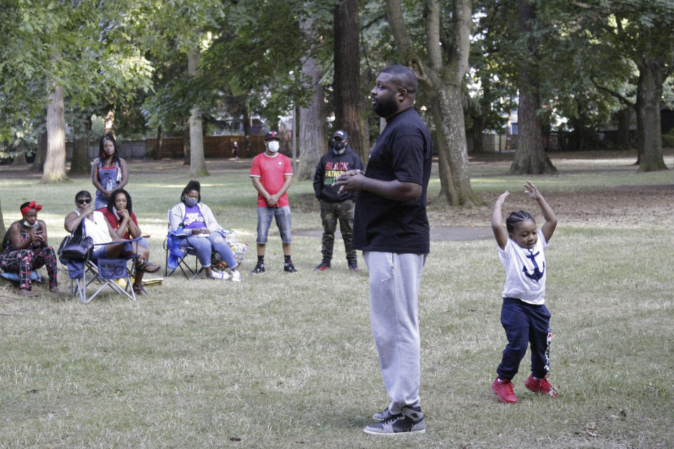 Sam Thompson, founder of Black Men and Women United, speaks to members of the Black community during a weekly meeting as his 3-year-old son, Jet, plays behind him in Portland, Ore., on Wednesday, Aug. 12, 2020. Thompson founded the group amid the ongoing protests in Portland with the goal of bringing long-term resilience to the city's Black community, which has endured years of racism. (AP Photo/Gillian Flaccus)