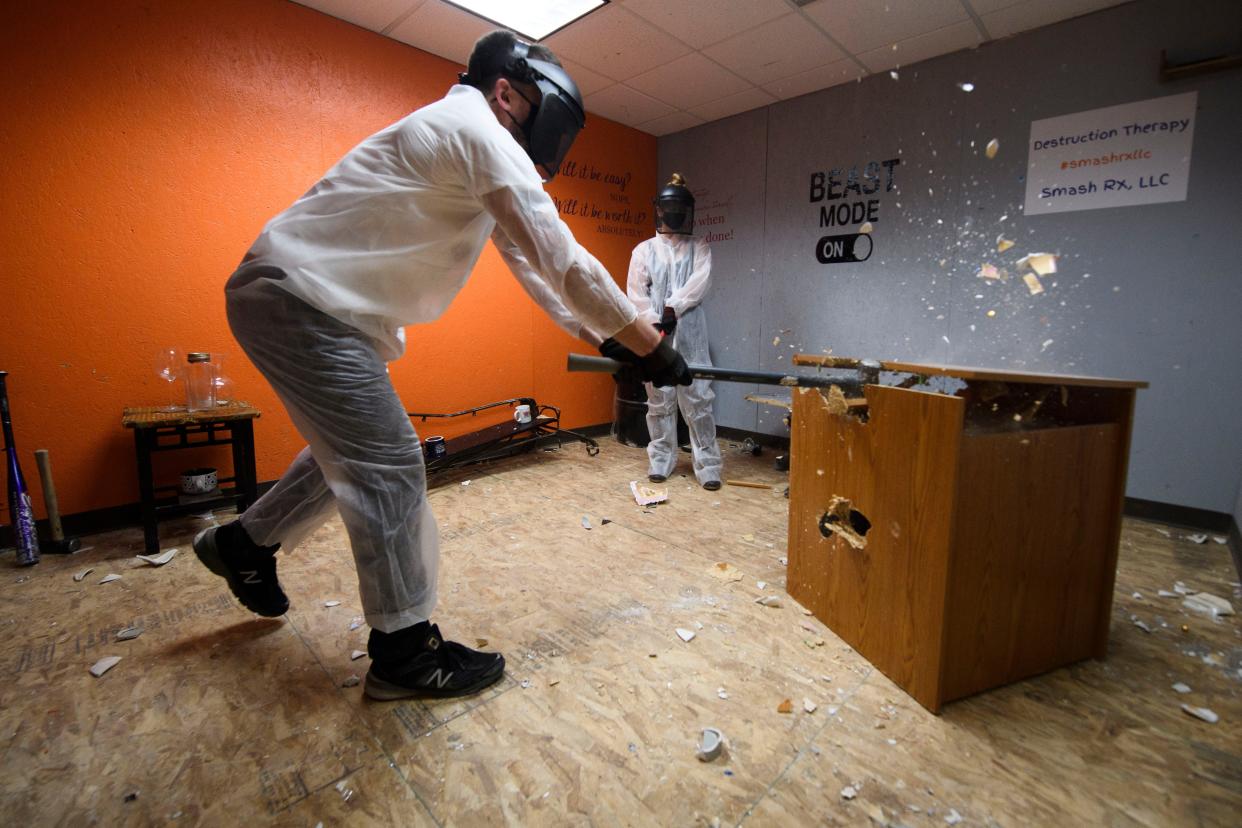 A man brings down a sledgehammer on a wooden cabinet in a rage room in February 2021.