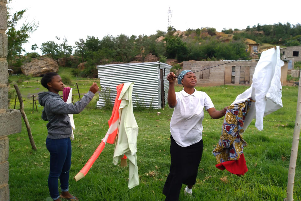 Matefo Litali (der) y su hija Refiloe recogen ropa que se secó al sol en su casa de Ha Thetsane, en Maseru, Lesotho, el 12 de diciembre del 2020. Litali fue despedida por la fábrica textil donde trabajaba ante la escasez de pedidos por la pandemia del coronavirus. (Neo Ntsoma/The Fuller Project via AP)