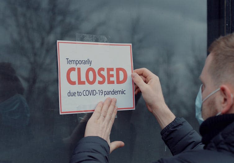 Man putting up a sign saying temporarily closed because of COVID.