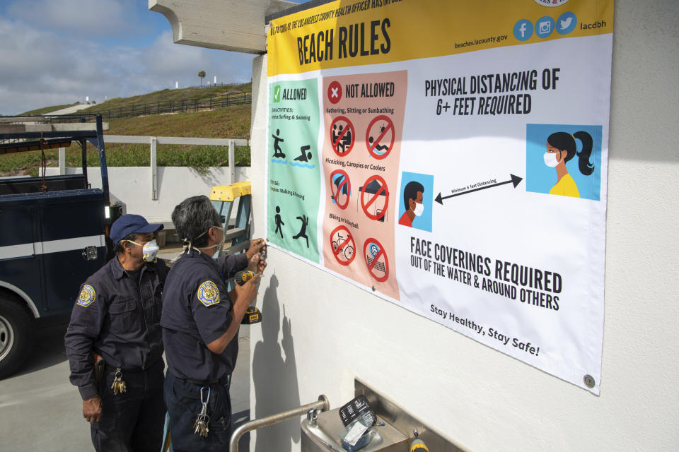 In this Tuesday, May 12, 2020, photo provided by Los Angeles County, Los Angeles County Department of Beaches & Harbors marina maintenance workers Leonel Salcedo, left, and David Henriquez install a new beach rules sign showing that masks and social distancing are required, at Torrance Beach in Torrance, Calif., for Wednesday's reopening of the beaches. Masks are required at Los Angeles County beaches, which reopened Wednesday, May 13, 2020, to join counterparts in other states that have allowed a somewhat limited return to famed stretches of sand. (Michael Owen Baker/Los Angeles County via AP)