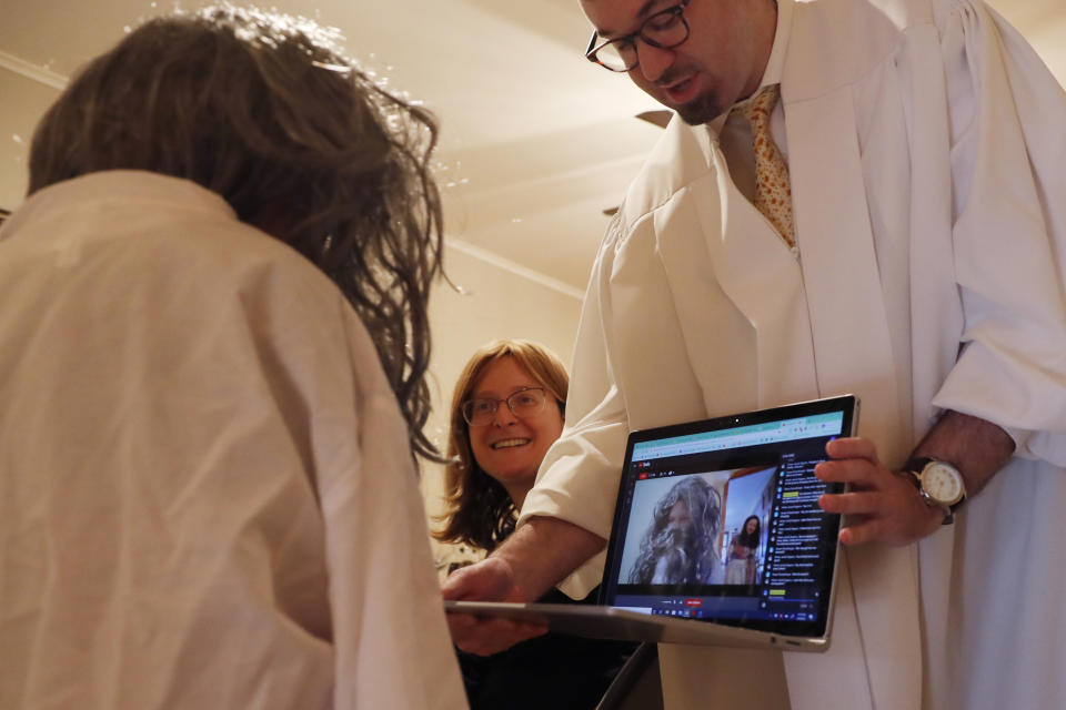 Rabbi Shlomo Segal, right, holds his laptop so participants see his daughter Rayna, 8, left, dressed in a white robe and wig as the prophet "Elijah" during a virtual Passover seder, Wednesday, April 8, 2020, in New York, in the Sheepshead Bay section of Brooklyn, as the coronavirus outbreak and social distancing rules continue. Accoring to Jewish tradition, Elijah will arrive as an unknown guest to herald the advent of the Messiah. During the seder dinner, biblical verses are read while a door is briefly opened to welcome Elijah, who it is believed will appear and usher in the era of the Messiah. The seder commemorates Jews' historical redemption from Egyptian bondage, but also foretells their future redemption. (AP Photo/Kathy Willens)