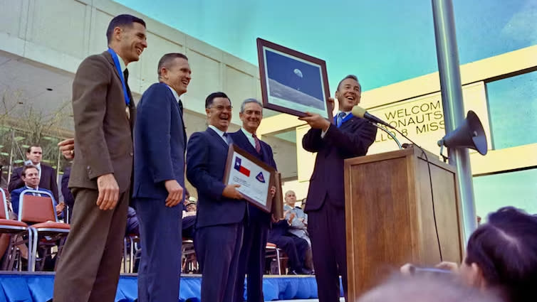 Astronauts in suits hold a photograph of the earth above the moon