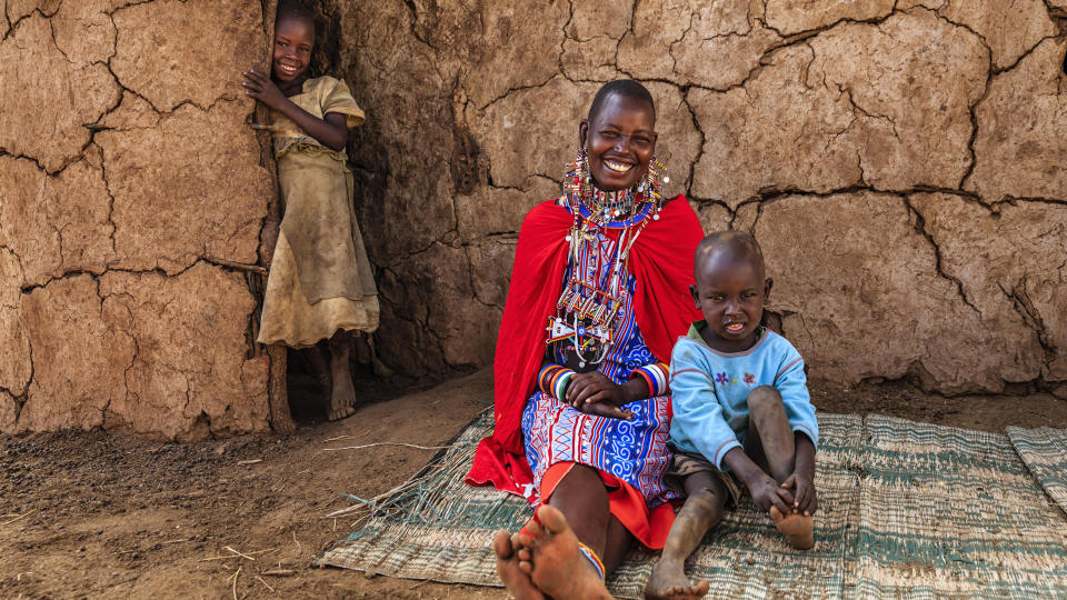 African mother from a Maasai tribe sitting with her baby next to her hut in Kenya, Africa.