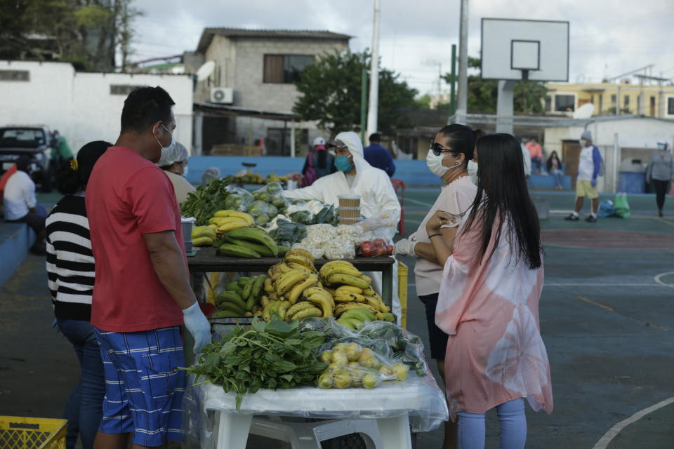 In this May 2, 2020 photo, local farmers, wearing protective as a measure to curb the spread of the new coronavirus, sell their products to residents, in San Cristobal, Galapagos Islands, Ecuador. For many islanders, the pandemic has left them to meditate on their relationships with nature, industry and travel. Some wonder if they should continue to remain so dependent on tourism, while others say it highlights the need for self-sufficiency. (AP Photo/Adrian Vasquez)