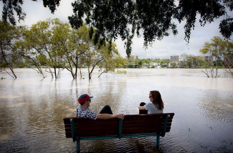 Two people sit on a bench surrounded by floodwaters after the Brisbane River broke its banks at West End in Queensland's state capital Brisbane on January 28, 2013. Deadly floodwaters were sweeping down Australia's east coast Tuesday, with Brisbane bracing for its river to peak as other towns waited anxiously as waters rose