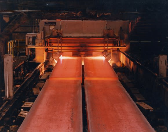 Hot steel sheets rolling out of oven furnaces along a conveyor belt.