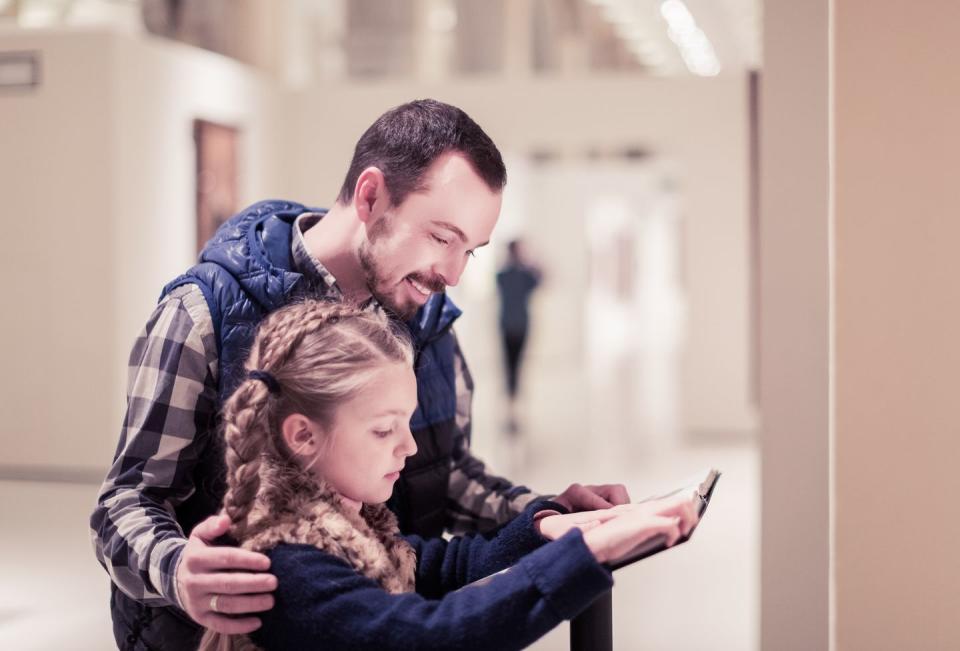 smiling father and daughter reading guide during visit to museum