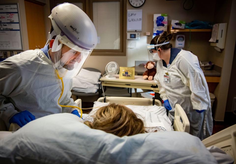 Dr. Tamim Mahayni listens to a patient's chest while nurse Abbey Malone looks at the patient's family photo in the ICU.