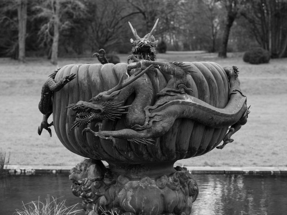 A black and white photo of a large sculpture featuring dragons twisting around a central water bowl.