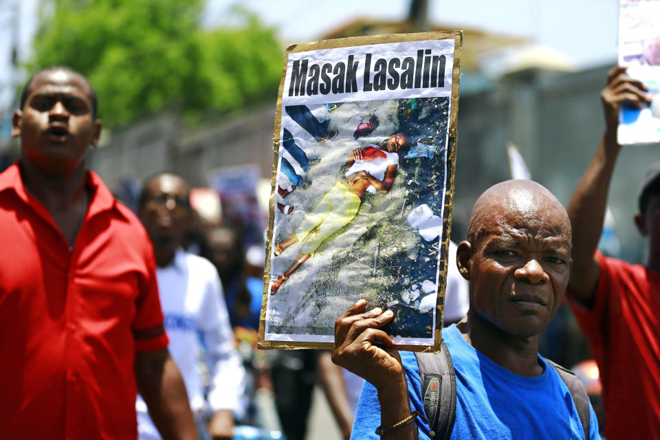 In this May 14, 2019, photo, a protester holds up a banner that reads in Creole "La Saline's massacre" in Port-au-Prince, Haiti. An internal report by the Haitian police Bureau of Criminal Affairs obtained by The Associated Press recommends that authorities arrest Jimmy Cherizier and 75 other people on charges including murder and rape. (AP Photo/Dieu Nalio Chery)