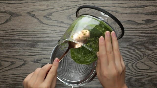 Pouring blended pandan pulp from food processor into metal strainer