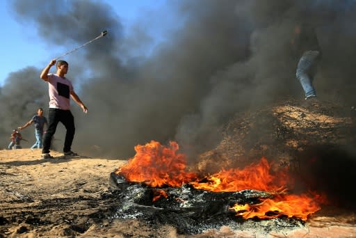 A Palestinian protester uses a slingshot next to burning tyres along the Israel-Gaza border on August 10, 2018