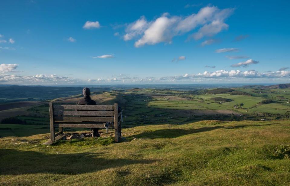 A hiker sits on a bench looking out over the mid-Wales countryside from Corndon Hill