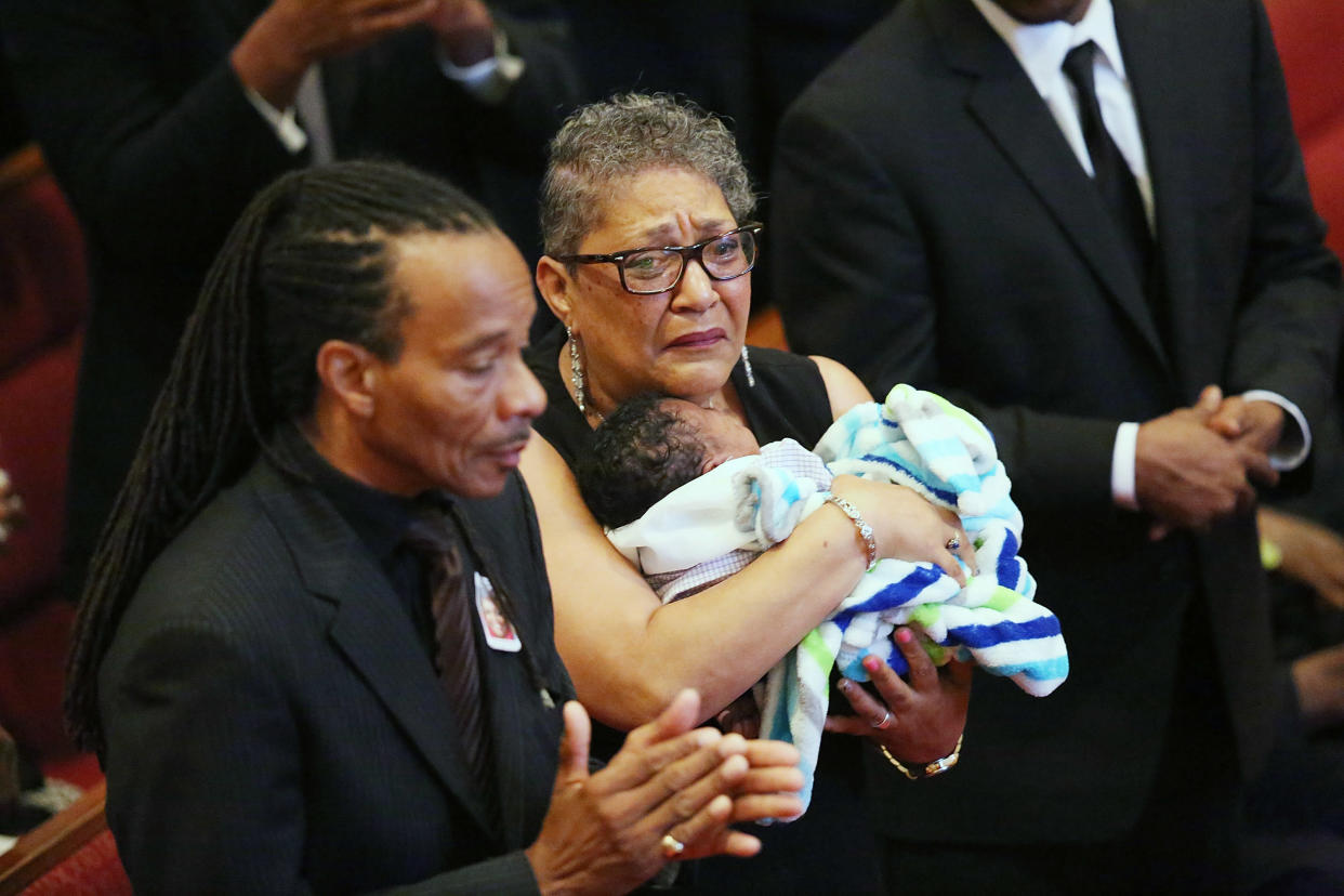 Sharon Risher, wearing black and holding a baby, attends what appears to be a funeral service, surrounded by several others.