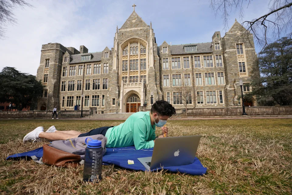 Masked to protect against the coronavirus disease (COVID-19) graduate student Jakob Burnham studies on a blanket in front of Georgetown University&#39;s White-Gravenor Hall on a warm and sunny day in Washington, U.S., March 9, 2021.  REUTERS/Kevin Lamarque