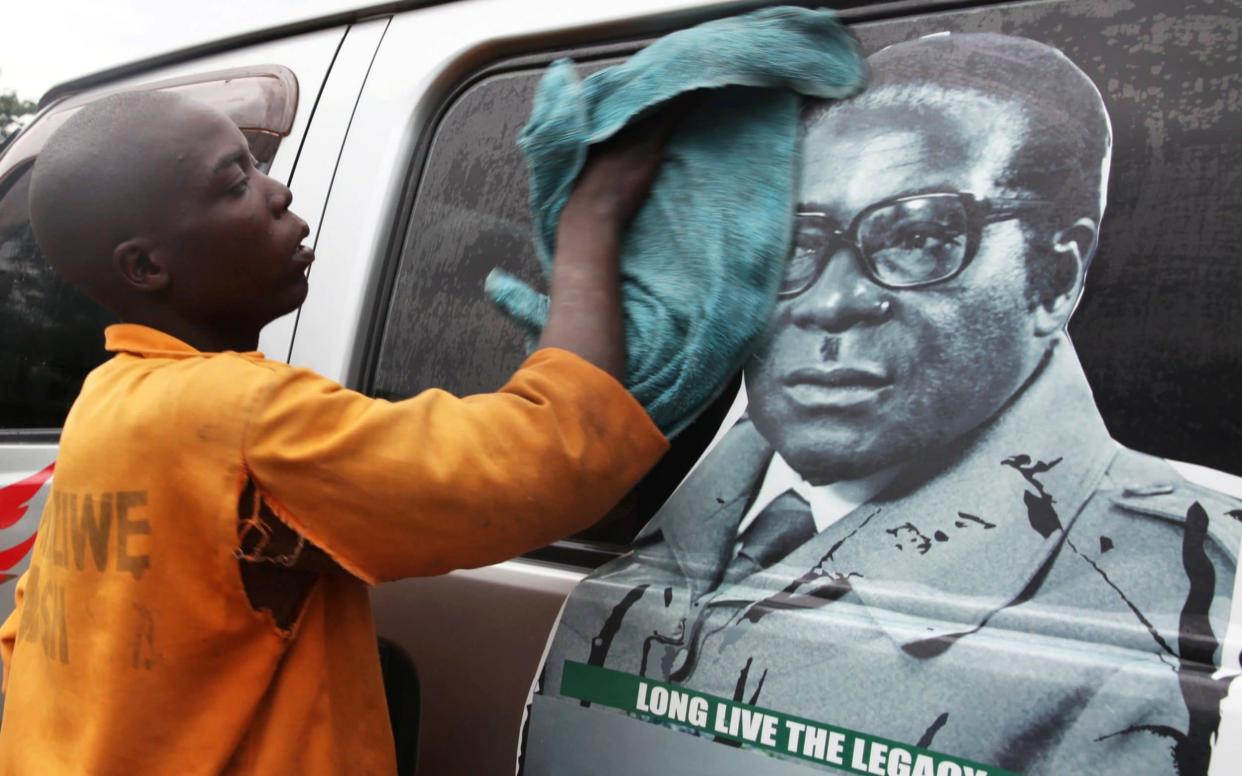 A young man in Harare washes a minibus adorned with picture of President Robert Mugabe - REUTERS