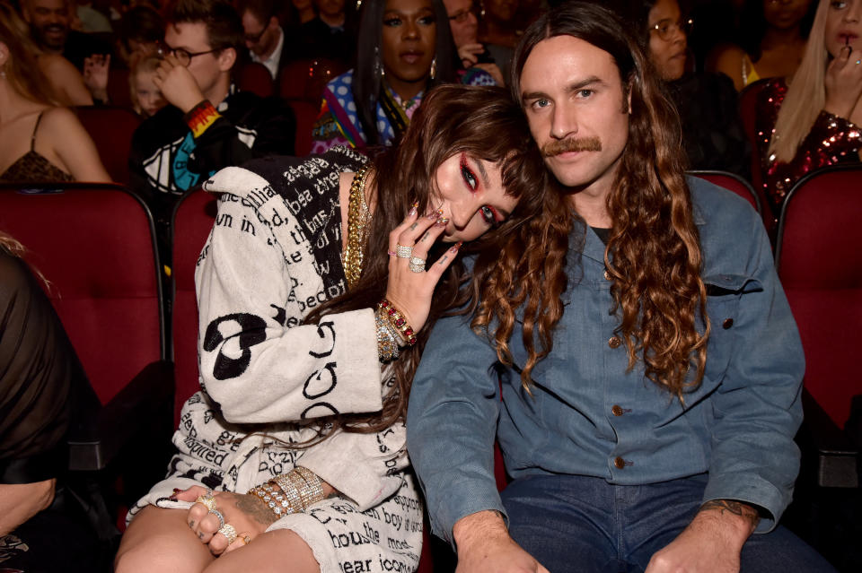 Kesha hiding half her face and leaning her head on Brad's shoulder as they sit in the audience