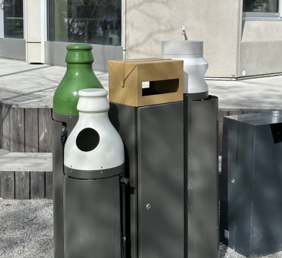 The tops of the recycling bins are decorated with a glass bottle, plastic cup, and cardboard box to indicate which items go in which bin