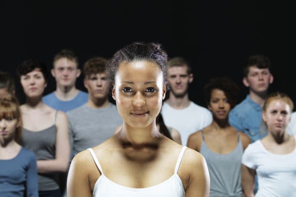 Happy young person in front of a group of young people. The background is dark. Neutral colors Happy young person in front of a