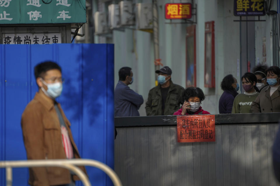 FILE - A woman wearing a face masks talks on her phone as masked residents stand near the metal barriers set up in their locked down neighborhood as part of COVID-19 controls in Beijing, Thursday, Nov. 10, 2022. (AP Photo/Andy Wong, File)