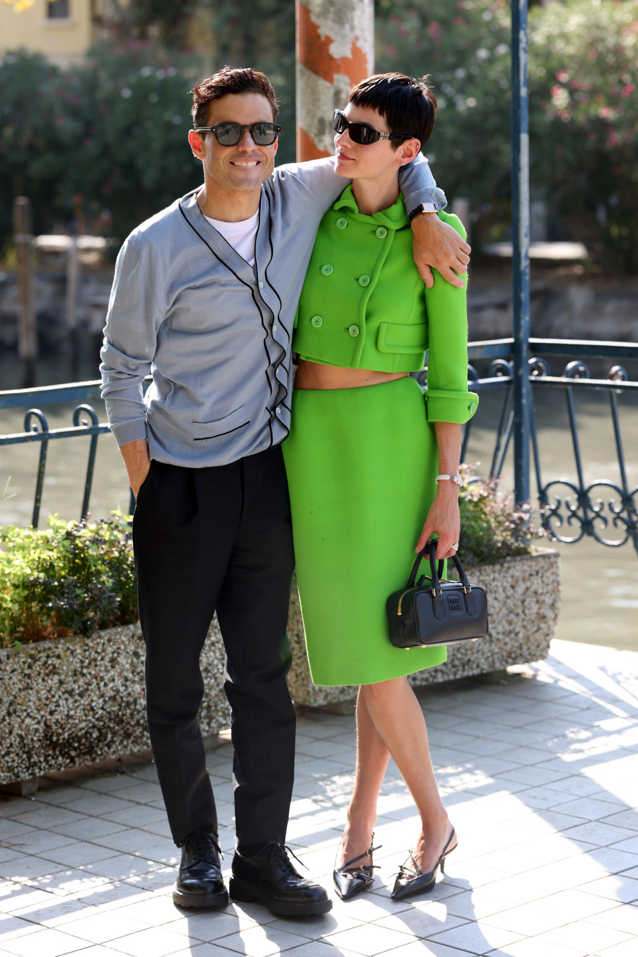 Rami Malek smiles for the camera as he stands with his arm around Emma Corrin's shoulders.