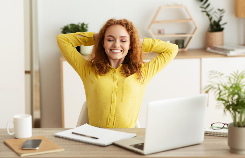 Happy creative designer stretching with closed eyes, working on laptop computer in office work