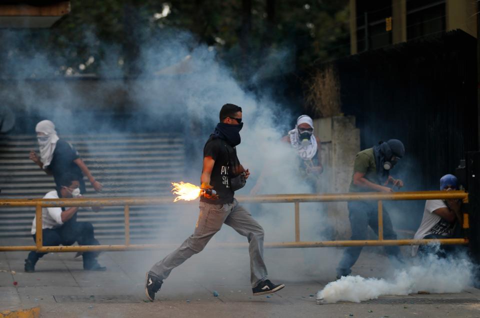 A demonstrator runs to throw a molotov bomb against Bolivarian National Police officers during clashes in Caracas, Venezuela, Thursday, March 6, 2014. A National Guardsman and a civilian were killed Thursday in a clash between residents of a Caracas neighborhood and armed men who tried to remove a barricade, Venezuelan officials said. (AP Photo/Fernando Llano)