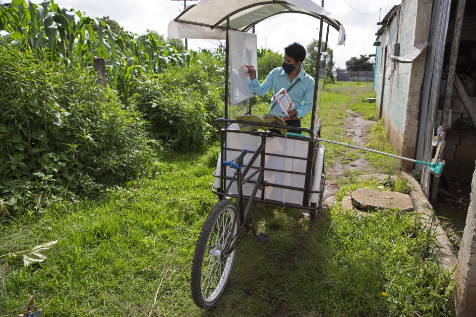 Teacher Gerardo Ixcoy conducts a math class from a secondhand, adult tricycle that he converted into a mobile classroom, in Santa Cruz del Quiche, Guatemala, Wednesday, July 15, 2020, amid the new coronavirus pandemic. The 27-year-old teacher deploys a sponge mop to serve as a safe distance reminder between him and his students. (AP Photo/Moises Castillo)