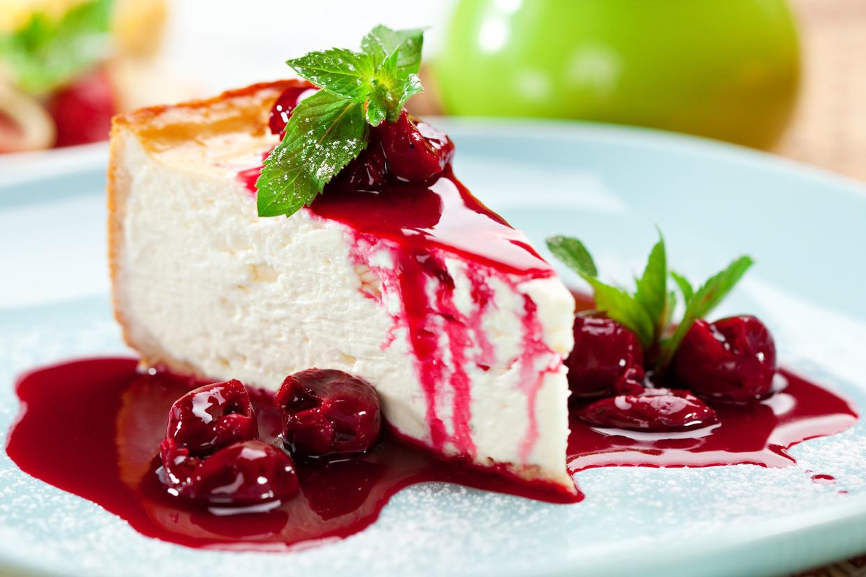Closeup of no-bake cheesecake with cherries and cherry syrup on top and around it, on a light blue plate, selective focus, with a blurred background
