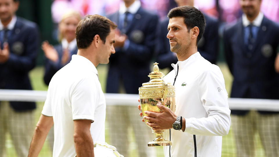 Novak Djokovic carries the Wimbledon trophy and passes Roger Federer.