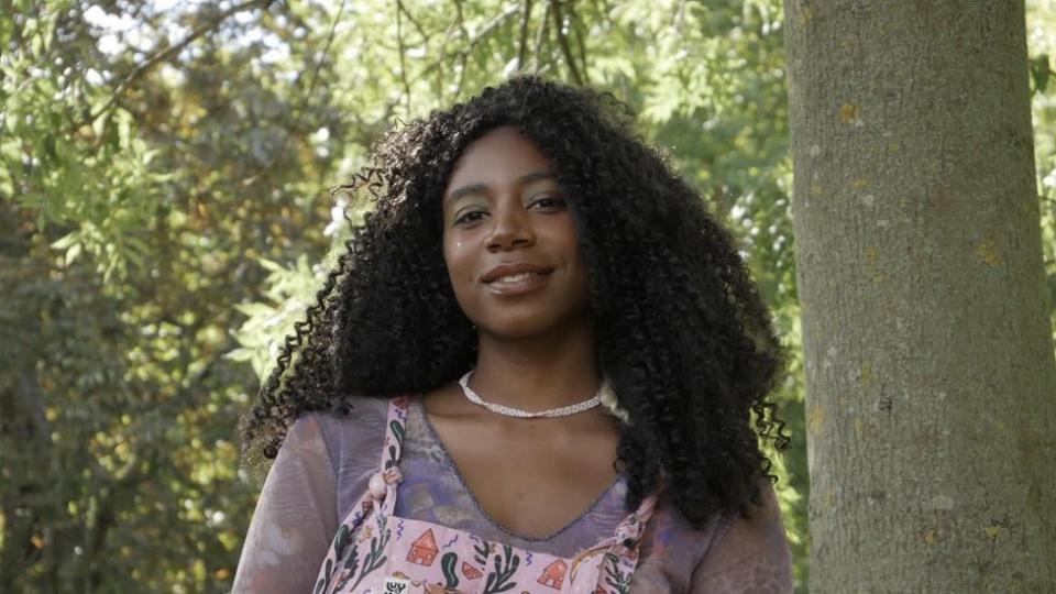 Dominique Palmer, climate justice activist, standing under the trees