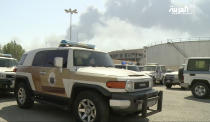 In this image made from a video broadcast on the Saudi-owned Al-Arabiya satellite news channel on Saturday, Sept. 14, 2019, a Saudi police cruiser sits in a parking lot as the smoke from a fire at the Abqaiq oil processing facility can be seen behind it in Buqyaq, Saudi Arabia. Drones launched by Yemen's Houthi rebels attacked the world's largest oil processing facility in Saudi Arabia and another major oilfield Saturday, sparking huge fires at a vulnerable chokepoint for global energy supplies. (Al-Arabiya via AP) TV OUT NO SALES