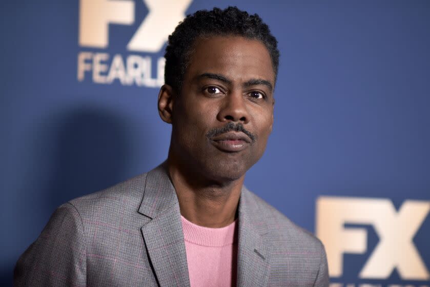 A man with short black hair and a thin mustache posing in a gray suit with a pink shirt