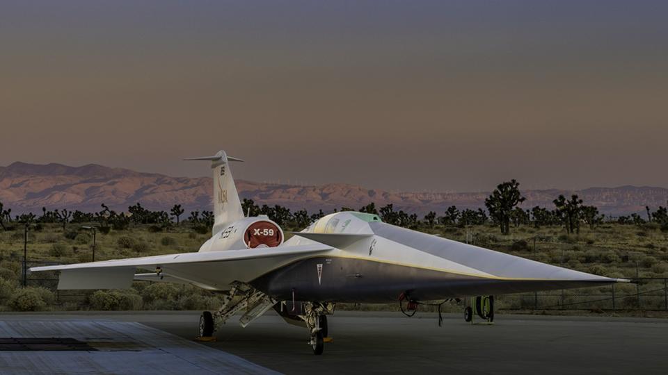 an elongated jet sits on a runway with mountains in the background