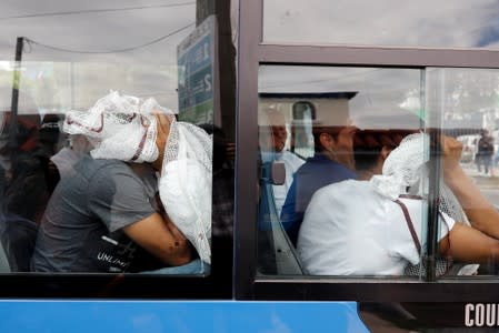 Guatemalan migrants cover their faces with their belongings while sitting on a bus in Guatemala City