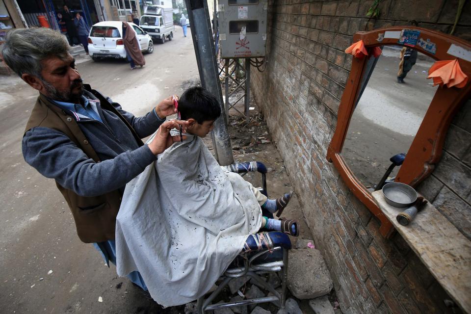 A barber gives a haircut to a customer at a roadside shop during World AIDS Day in Peshawar, Pakistan, 01 December 2020. According to doctors, cuts from razor blades that haven’t undergone proper sterilization are among some of the main causes of AIDS spread. World AIDS Day, observed annually on 01 December, is dedicated to raising awareness against the spread of AIDS and HIV infections.  (EPA/ARSHAD ARBAB)EPA