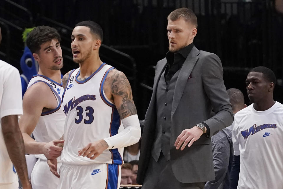 Washington Wizards center Kristaps Porzingis wears a suit while standing at the bench with forward Kyle Kuzma (33) and other teammates during the first half of an NBA basketball game against the Dallas Mavericks in Dallas, Tuesday, Jan. 24, 2023. (AP Photo/LM Otero)