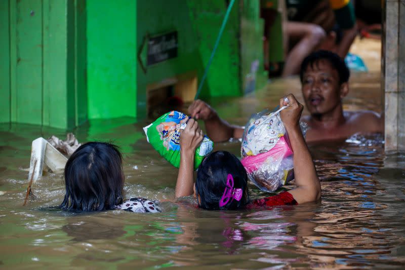 Women carry diapers as they cross an area flooded after heavy rains in Jakarta