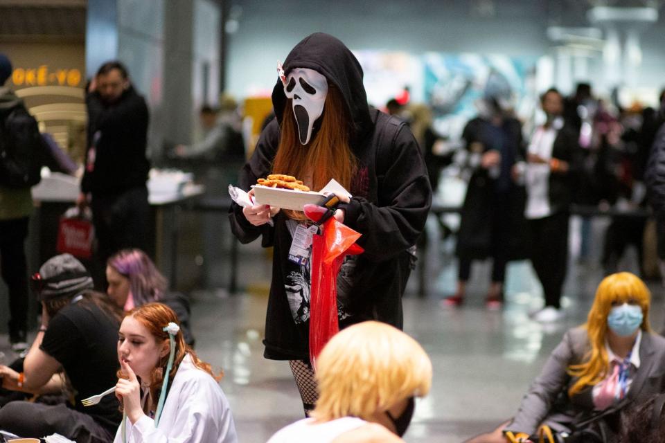 An attendee wearing a "Scream" mask at Anime NYC holds a tray of food