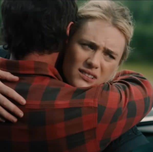 A man in a plaid shirt hugs Mackenzie Davis next to a car in an emotional outdoor scene