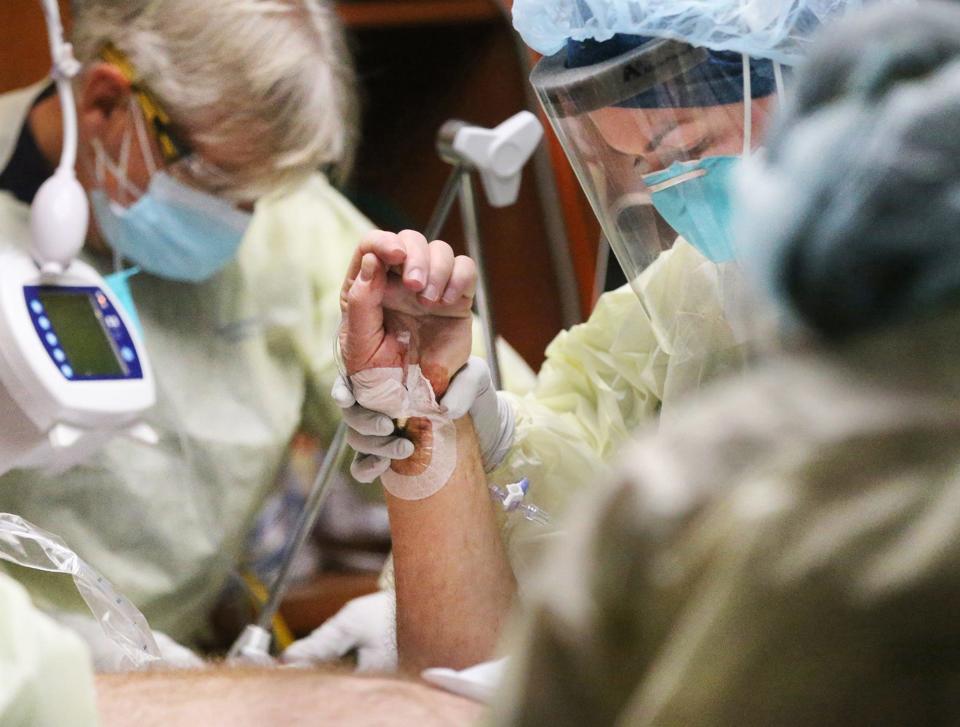 Registered nurse Becky Roy holds the arm of a COVID-19 patient at Wentworth-Douglass Hospital as respiratory therapist Philip Hosmer, left, and the rest of a team assist in flipping the patient to help his breathing.