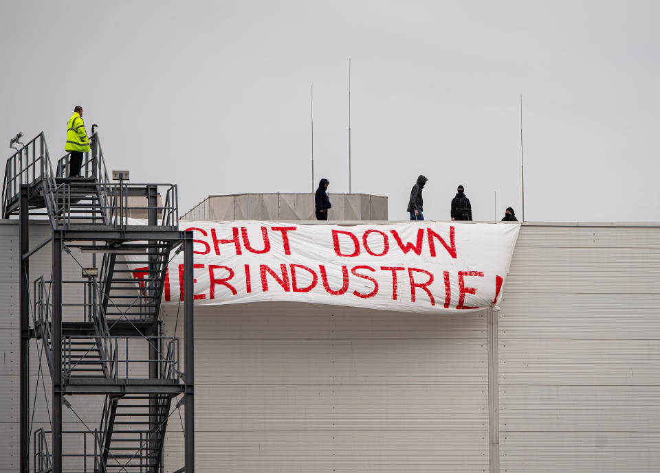 dpatop - 04 July 2020, North Rhine-Westphalia, Rheda-Wiedenbrück: Four activists of the "Alliance Together Against the Animal Industry" occupied a roof of the Tönnies company and hung up a banner from there with the inscription: "SHUT DOWN ANIMAL INDUSTRY". On the left, an employee of Tönnies Security is standing on the staircase to the roof. Photo: Guido Kirchner/dpa (Photo by Guido Kirchner/picture alliance via Getty Images)