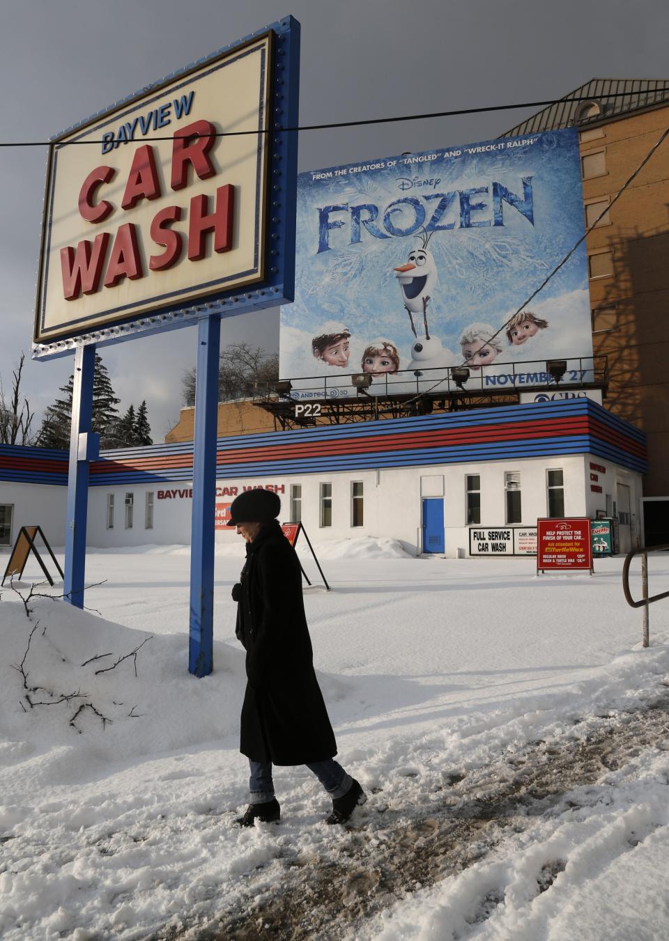 A woman trudges past a car wash and a sign advertising the Disney animated film "Frozen" after a fresh snowfall in Toronto