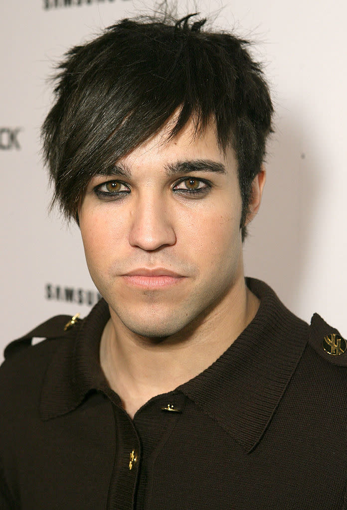 Pete with styled hair and eyeliner, wearing ashirt with gold details, looking at the camera