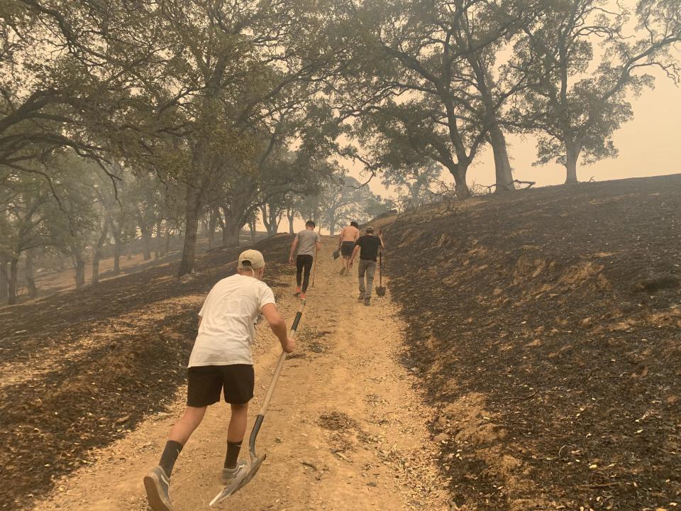 A family works to cut a fire line to save their home and other residences in a California neighborhood as several wildfires ravage the state. / Credit: Zach Galgan