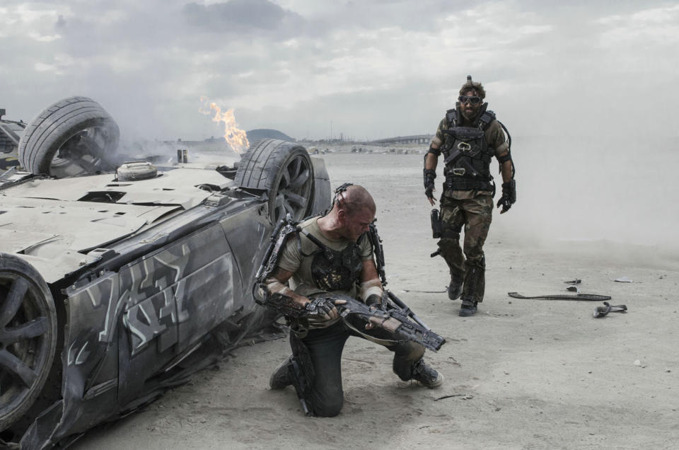 A man in a robotic exoskeleton attempts to reload his weapon before an assailant can reach him in “Elysium”