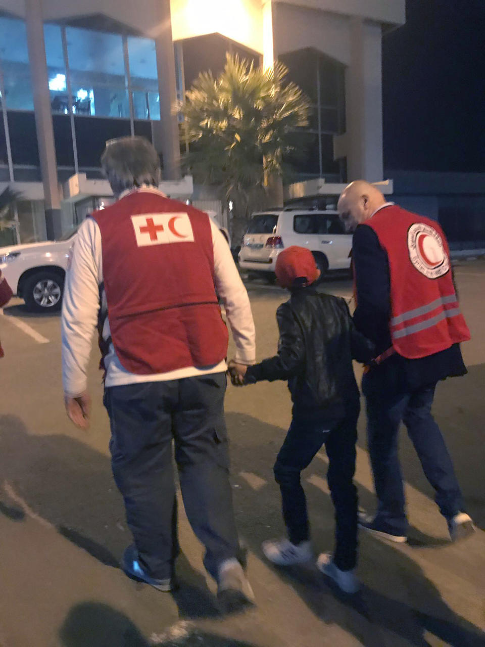 In this photo taken Wednesday, Nov. 6, 2019, Alvin, an 11-year-old Albanian boy who was taken to Syria by his mother when she joined the Islamic State group, is accompanied to Damascus airport by Red Cross and Red Crescent officials, after he was freed from a crowded detention camp. The boy, who found himself with no family in the al-Hol camp run by Kurdish forces in northeastern Syria after his mother and siblings died amid fighting, is heading home, to Italy, where his father lives. (International Federation of Red Cross and Red Crescent photo via AP)