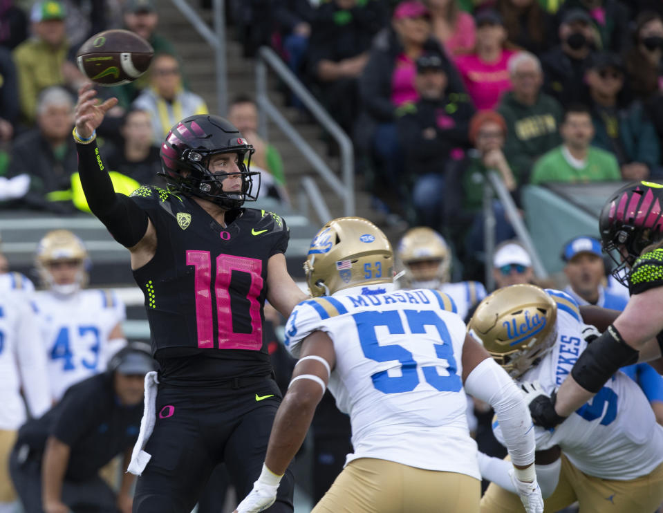 Oregon's Bo Nix, left, throws down field ahead UCLA's Darius Muawai during the first half in an NCAA college football game Saturday, Oct. 22, 2022, in Eugene, Ore. (AP Photo/Chris Pietsch)